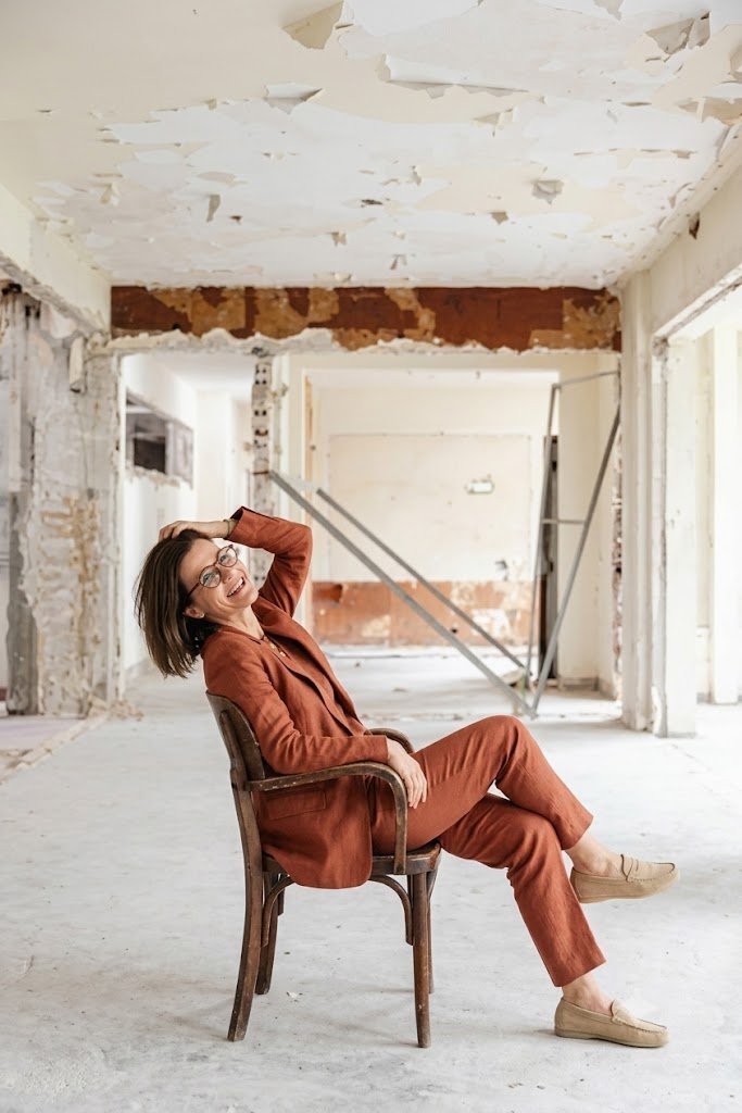 Mabel Rocha sentada em uma obra, de terno terracota